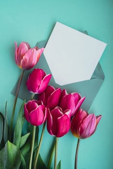 Empty white envelope copy space for your text or design with beautiful pink tulip bouquet on green background. Template mock up for holiday spring greeting card. Top view Flat lay blank paper Feminine concept postcard. Creative minimalistic