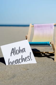 ALOHA BEACHES text on paper greeting card on background of beach chair lounge summer vacation decor. Sandy beach sun. Holiday concept postcard. Travel Business concept