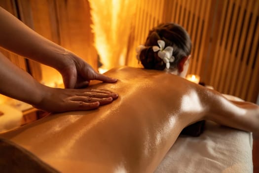 Closeup woman customer enjoying relaxing anti-stress spa massage and pampering with beauty skin recreation leisure in warm candle lighting ambient salon spa at luxury resort or hotel. Quiescent