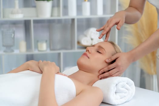 Caucasian woman enjoying relaxing anti-stress head massage and pampering facial beauty skin recreation leisure in dayspa modern light ambient at luxury resort or hotel spa salon. Quiescent