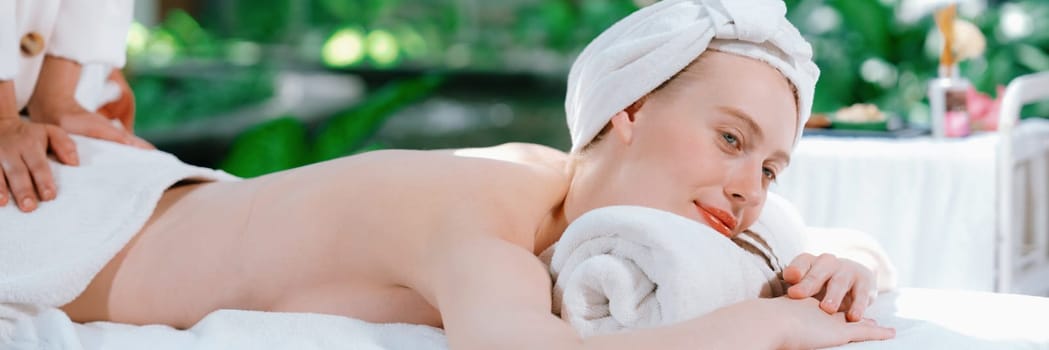 Beautiful young woman lies on white spa bed during having back massage. Attractive caucasian woman having back massage surrounded by natural environment. Relaxing and healthy concept Tranquility.