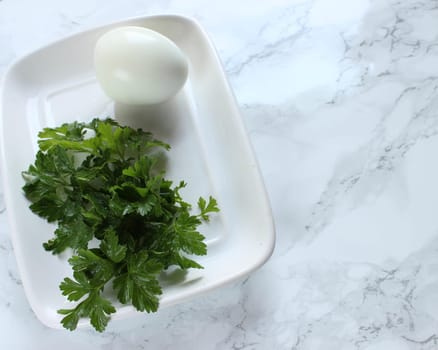 Boiled chicken egg and parsley on a white plate on a marble background. High quality photo