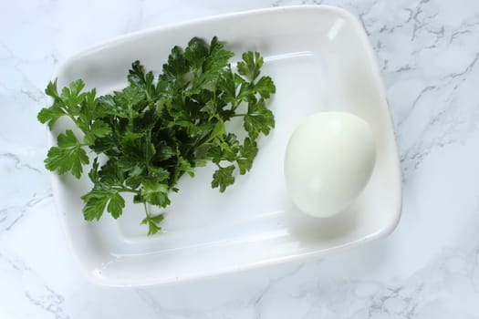 Boiled chicken egg and parsley on a white plate on a marble background. High quality photo