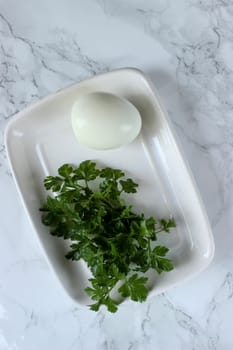 Boiled chicken egg and parsley on a white plate on a marble background. High quality photo