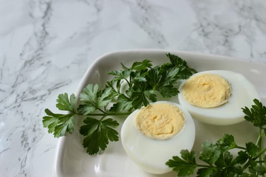 Boiled chicken egg and parsley on a white plate on a marble background. High quality photo