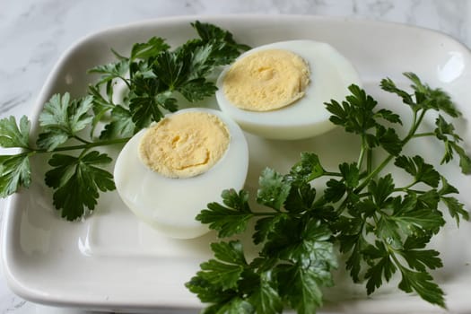 Boiled chicken egg and parsley on a white plate on a marble background. High quality photo