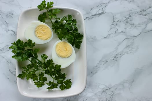 Boiled chicken egg and parsley on a white plate on a marble background. High quality photo