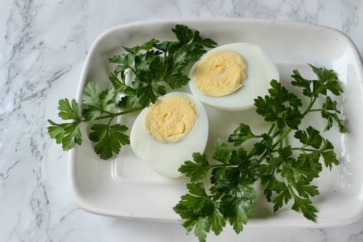 Boiled chicken egg and parsley on a white plate on a marble background. High quality photo