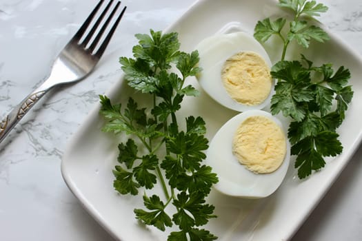 Boiled chicken egg and parsley on a white plate on a marble background. High quality photo