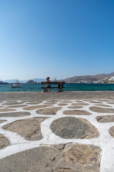 Woman waiting on a bench next to the port in Mykonos