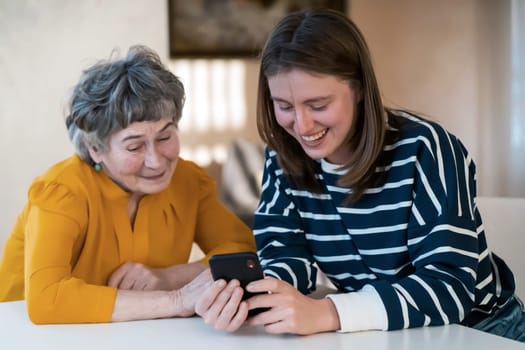 Young girl, a granddaughter, explains to an elderly relative how to use a smartphone and an application to communicate with a doctor at home. The family loves and cares for their elderly parents.