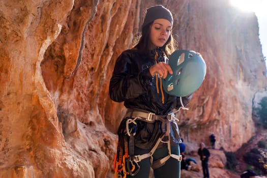 Young girl is preparing for training on the rocks, in the mountains and puts a helmet on her head for safety to protect her health, woman engaged in active sports, in mountaineering and rock climbing.