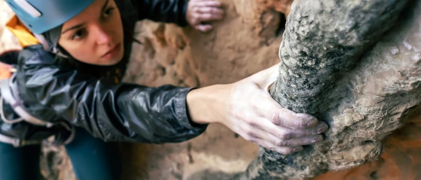 Young girl is engaged in extreme sports, fearlessly climbs up the rock using white magnesia powder, holds her hand to the ledge in the relief, close-up view, focus on the finger, the girl is blurred.