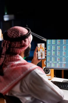 Middle Eastern man engrossed in a video conference call with a coworkers on his cell phone. Muslim guy uses wireless technology for work and research, showcasing his digital communication skills.