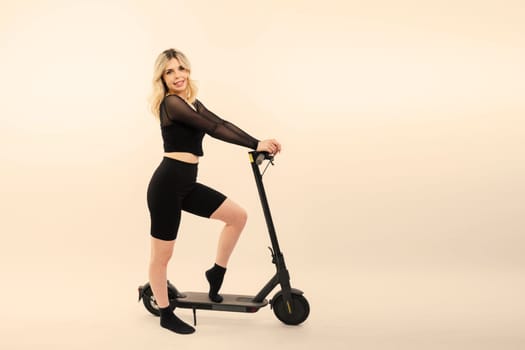 Young pretty smiling female in sport wear standing with electric scooter happily look in camera