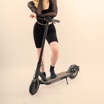Young pretty smiling female in sport wear standing with electric scooter happily look in camera
