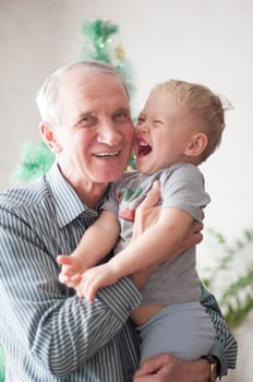 grandfather holds his grandson in his arms and both laugh against the background of a decorated Christmas tree, sweet home,High quality photo