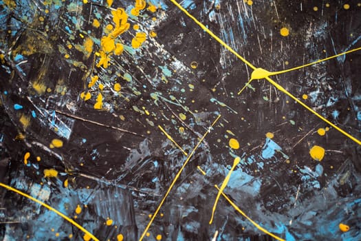 Abstract paint splash art yellow and blue in dark background. Artful painting is painted in colors by living person on black canvas. Dark canvas with colours randomly splattered on it