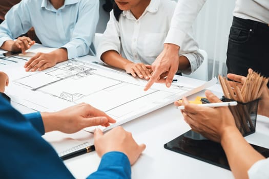 Diverse group of civil engineer and client working together on architectural project, reviewing construction plan and building blueprint at meeting table. Prudent