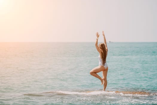 Woman sea yoga. Back view of free calm happy satisfied woman with long hair standing on top rock with yoga position against of sky by the sea. Healthy lifestyle outdoors in nature, fitness concept.