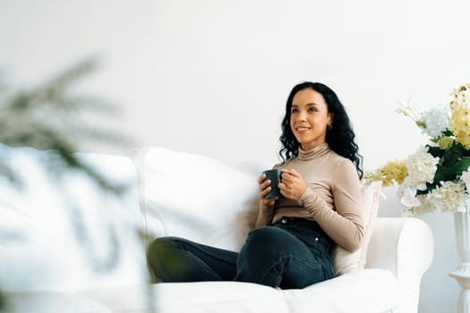 Happy woman drinking coffee on a sofa at home for crucial rest and relaxation. Portrait of young African American woman holding a cup.