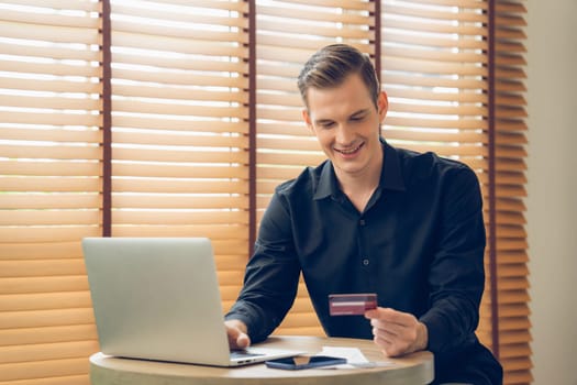 Young man using laptop with credit card for internet banking, online shopping E commerce by online payment gateway at home office. Modern and convenience online purchasing with debit card. Unveiling
