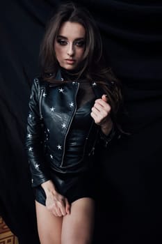 brunette in leather clothes in dark room on a black background