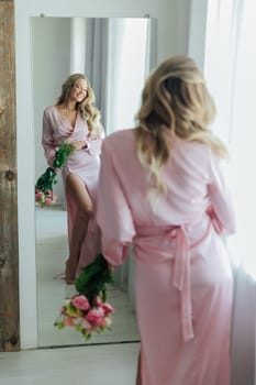 an elegant blonde woman with flowers looks in the mirror in the room