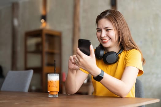 Asian woman wearing headphones listening to music on her smartphone relax in cafe.