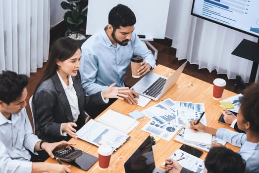 Top view multiracial analyst team use BI dashboard data to analyze financial report on meeting table. Group of diverse business people utilize data analysis by FIntech for business decision. Concord