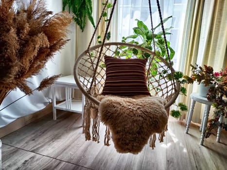 Modern cozy beautiful room with a braided rope macrame chair, green plants and a window with curtains. Interior and background. Location for photo shooting
