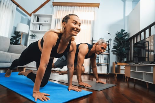 Athletic and active senior couple doing exercise on fit mat with plank climbing together at home exercise as concept of healthy fit body lifestyle after retirement. Clout