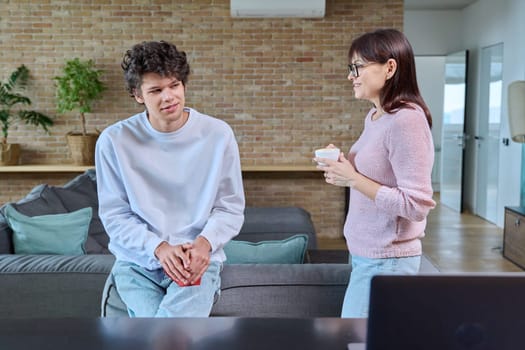 Middle aged mother and son 19, 20 years old talking together at home in living room. Family, relationships, communication mom teenage son, people concept