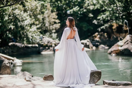 a beautiful woman in a long white dress looks into the distance at a beautiful lake with swans