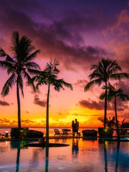 a couple of men and women watching the sunset on a tropical beach in Mauritius with palm trees by the swimming pool, Tropical sunset on the beach in Mauritius, a couple on a honeymoon trip
