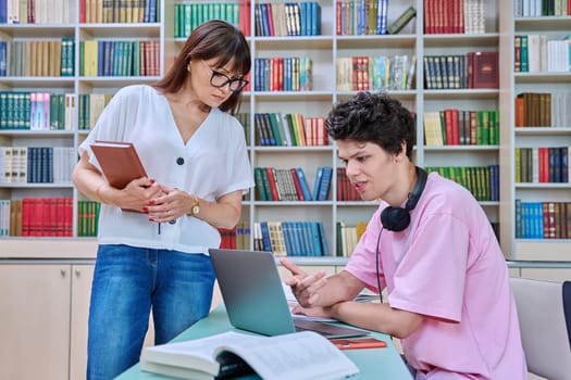 Woman teacher mentor talking teaching helping male student in college library, lesson, exam preparation. Knowledge, education, youth, college university concept