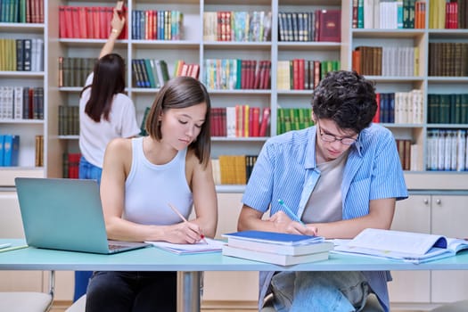 College students guy and girl study in library. Students prepare for an exam, write, read, and type on laptop. Education, knowledge, learning, youth concept