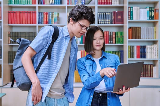 Young students male and female in college library talking, studying, preparing for exams, with laptop. Knowledge, education, youth, college university concept