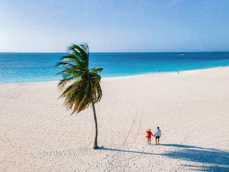 Eagle Beach Aruba Caribbean Island, Palm Trees on the shoreline of Eagle Beach in Aruba, a couple of men, and a woman on the beach of Aruba during sunset