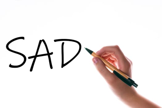 Children hand with pen write on a blue white background. Writing hand. Word SAD