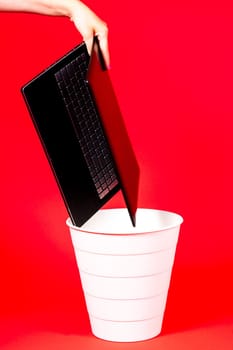 Black laptop in a trash bin on red background isolated