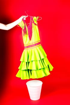 Shot of young woman hand throwing her outwear dress in the trash isolated on red background