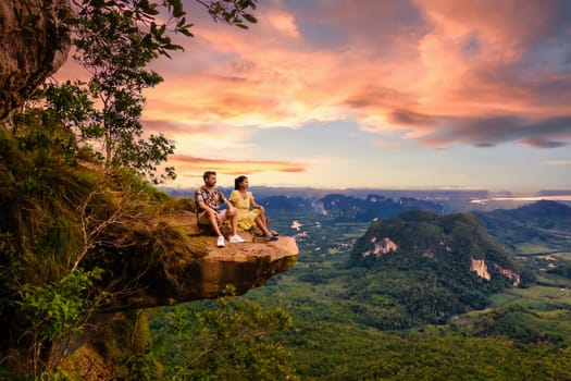 Couple at the edge of a mountain, Dragon Crest Mountain Krabi Thailand, Young travelers sit on a rock that overhangs the abyss, with a beautiful landscape. Dragon Crest or Khuan Sai at Khao Ngon Nak