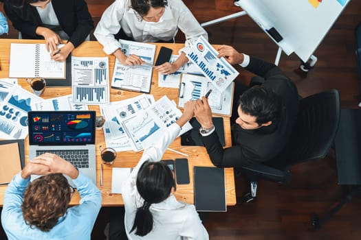 Wide top view of diverse group of business analyst team analyzing financial data report paper on meeting table. Chart and graph dashboard by business intelligence analysis. Meticulous