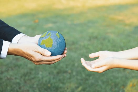 Businessman hand giving Earth globe to little boy as Earth day concept as corporate social responsible to contribute greener environmental protection for sustainable future generation. Gyre