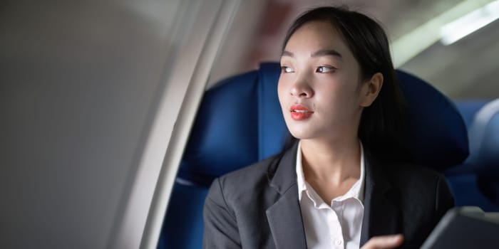 Successful Asian business woman, Business woman working in airplane cabin during flight on tablet.