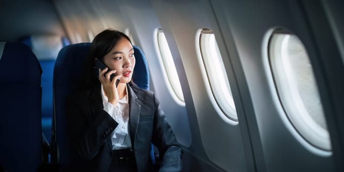 Successful Asian business woman, Business woman working in airplane on laptop computer and looking out the window along with talking on the phone.