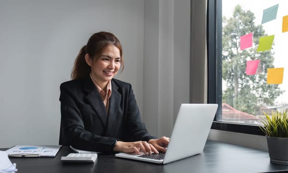 Professional Asian business woman intent on work focusing on laptop in modern office.