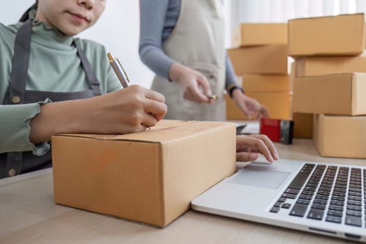 Two Asian entrepreneur women take order and check boxes of products according to customer orders in preparation for delivery..