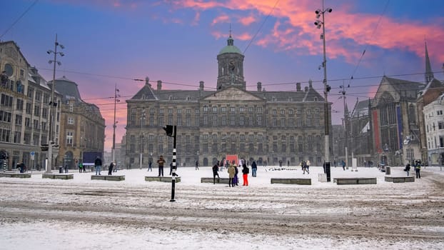 Snowy city Amsterdam at the Dam square in the Netherlands in winter at sunset